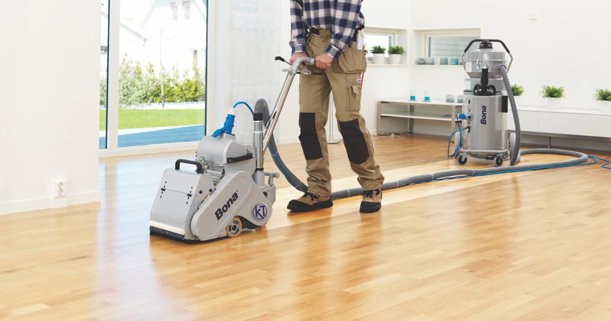 Technician guiding a Bona belt sander with dust-containment unit during Wood Floor Sanding of an engineered oak hardwood floor in a bright Tottenham living room.