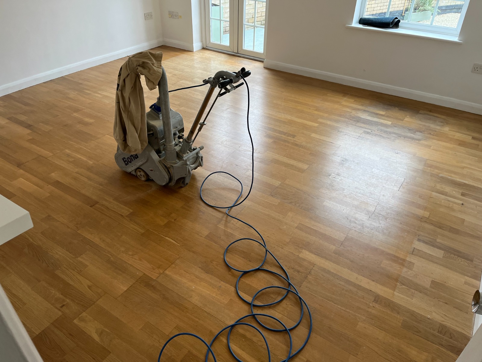 Wood Floor Sanding on Oak Strip Flooring in Tottenham – Mid-Project Snapshot Wood Floor Sanding machine in action on a honey-toned oak strip floor inside a bright Tottenham living room.