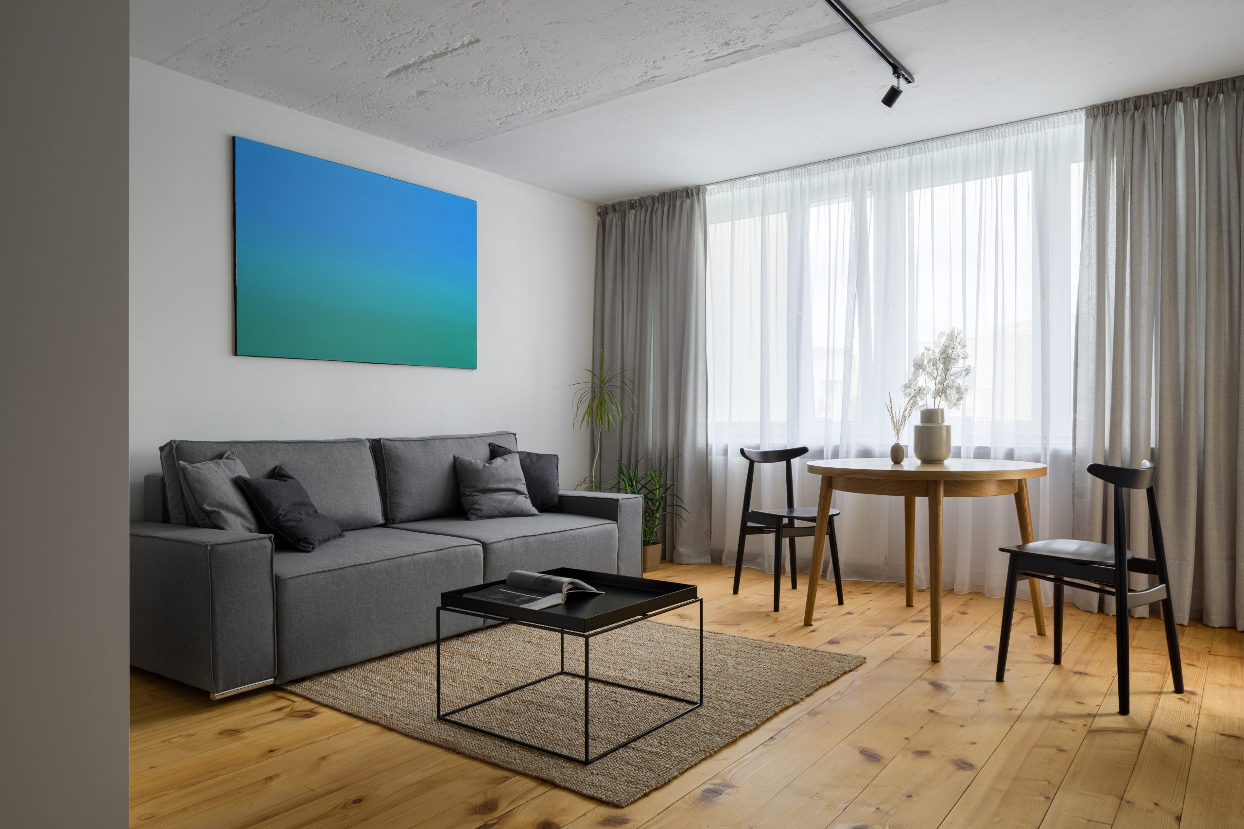  Wood Floor Sanding tottenham finish: light softwood pine floorboards in a stylish Tottenham living room featuring a grey sofa, round oak table and airy floor-to-ceiling curtains.