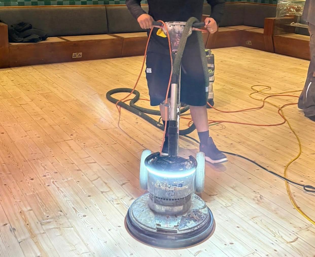  Wood Floor Sanding tottenham in action: a technician guides a rotary sander across wide softwood pine floorboards in a Tottenham commercial space.