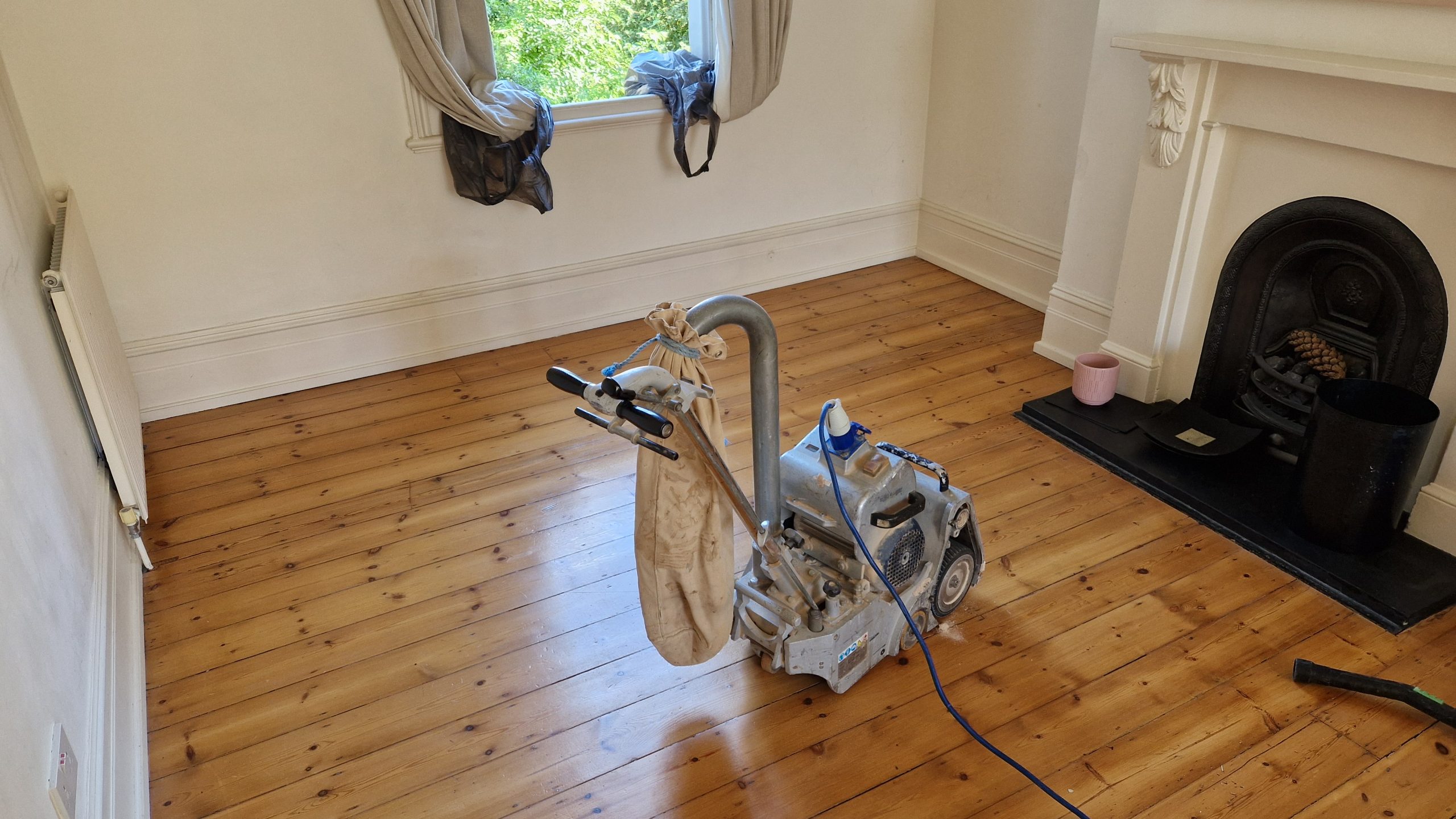 Wood Floor Sanding tottenham project: freshly sanded softwood pine floorboards in a Tottenham living room, with a drum sander beside a period fireplace.