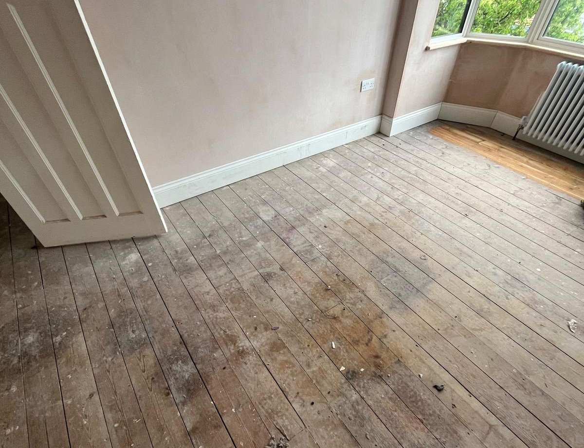 Wood Floor Sanding tottenham before shot: dusty, stained solid pine floorboards in a Tottenham bay-window bedroom awaiting restoration.