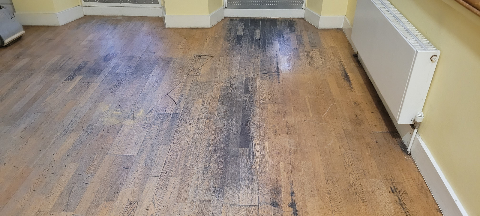 Badly worn oak strip hardwood floor in a Tottenham room, marked with dark traffic lanes and scratches awaiting professional Wood Floor Sanding.