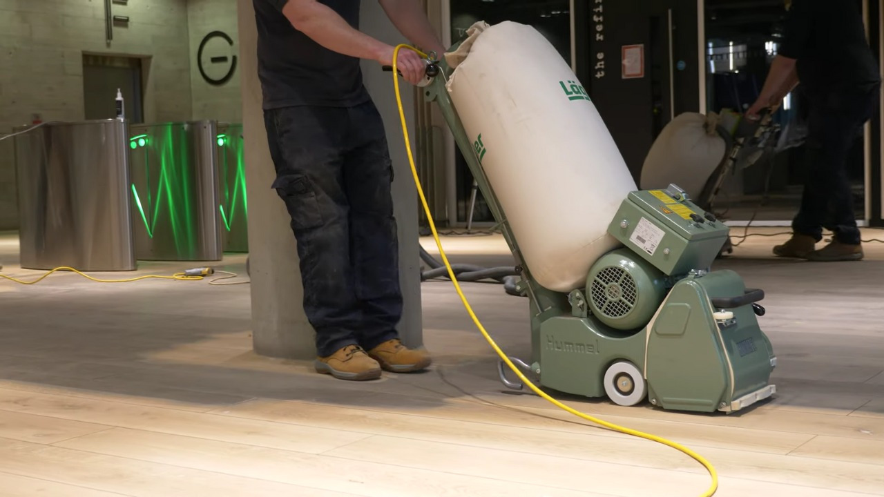 Commercial Floor Sanding in Tottenham on a light oak hardwood lobby floor, technician using a dust-extraction drum sander in a modern commercial entrance.