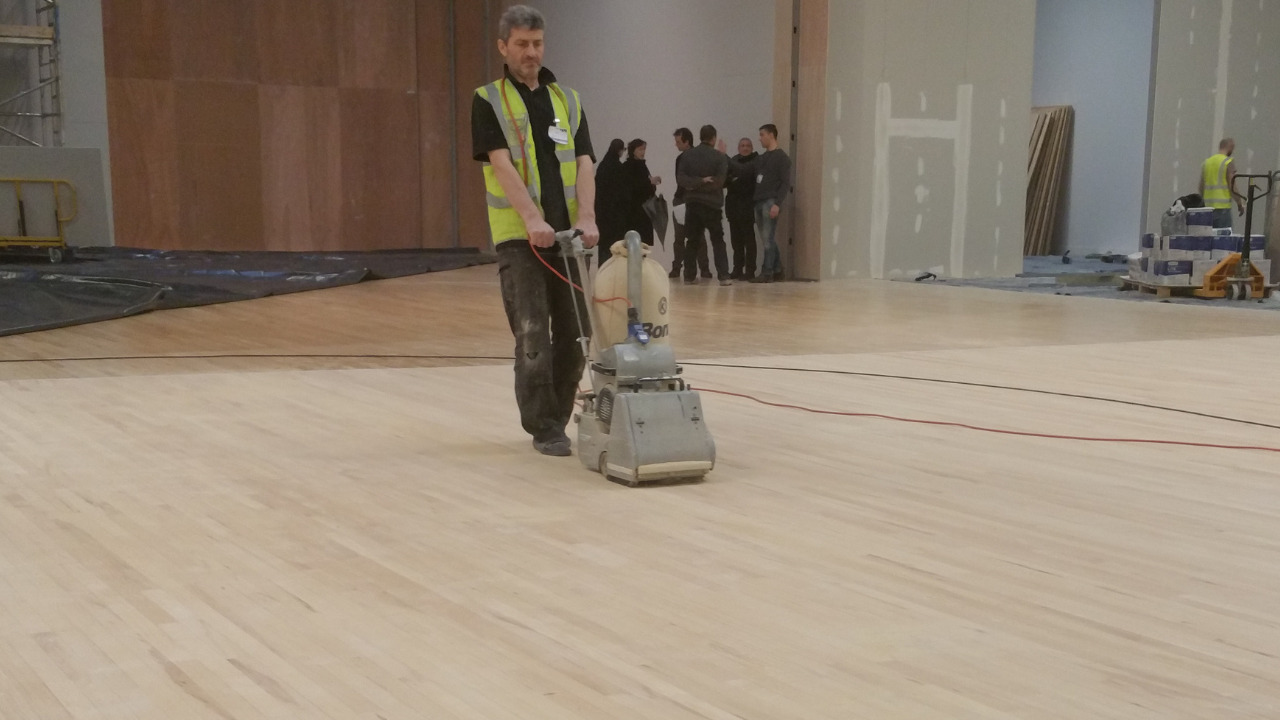 Commercial Floor Sanding in Tottenham on a maple hardwood sports hall floor, technician using a drum sander to smooth the newly laid surface.