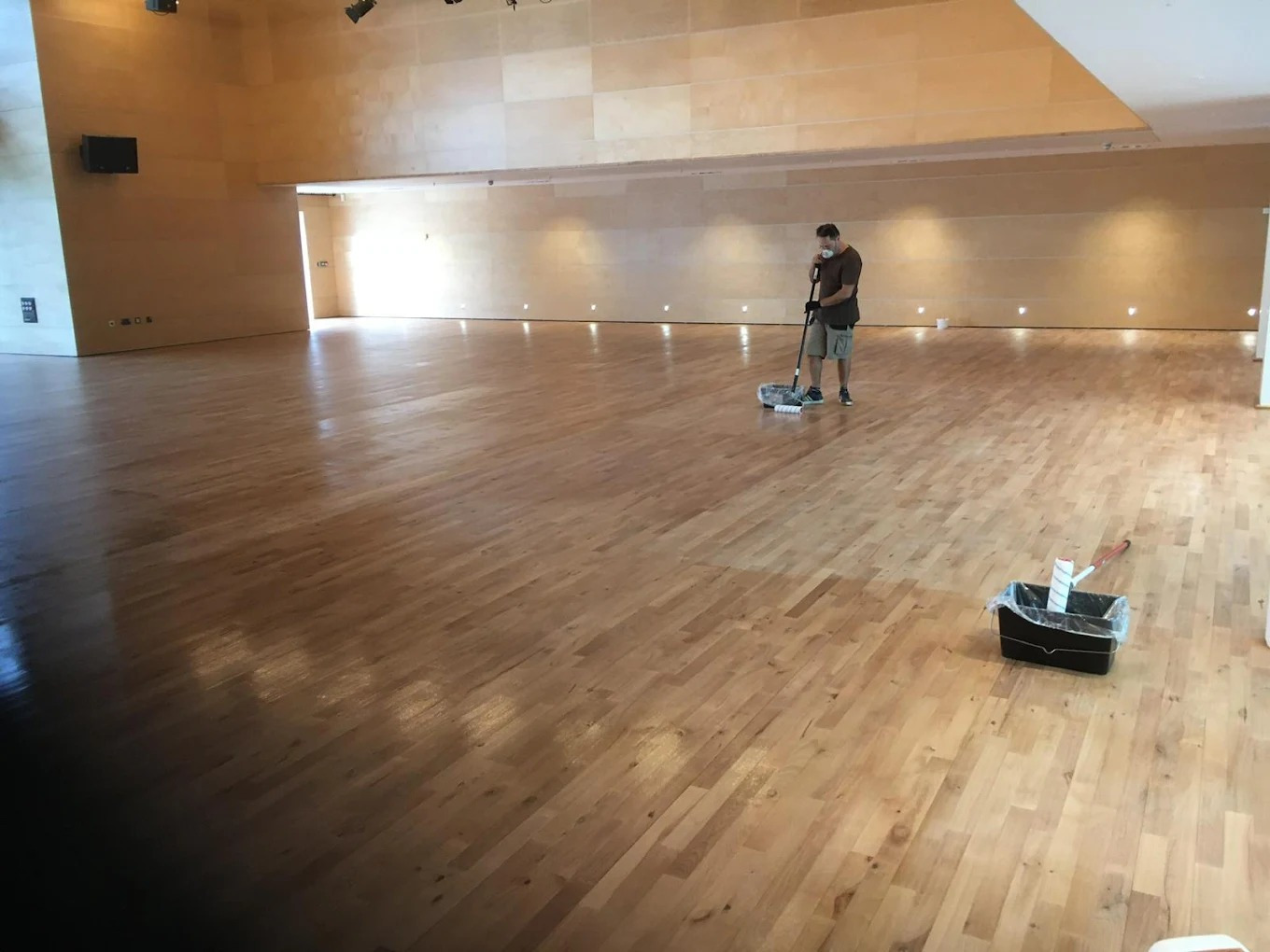 Technician carrying out Commercial Floor Sanding in Tottenham on a large oak hardwood hall floor, applying protective seal for a smooth, uniform finish.