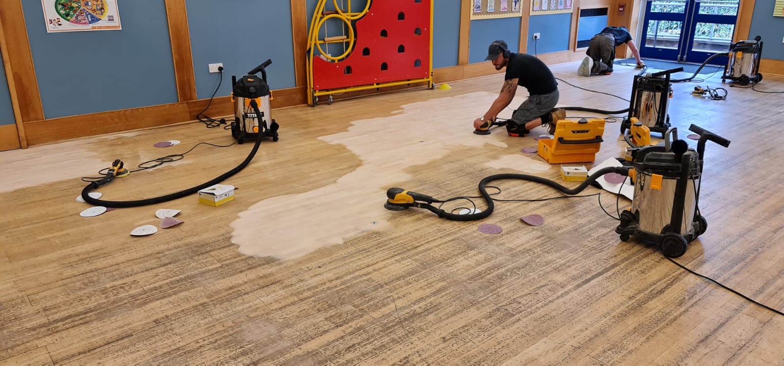 Commercial Floor Sanding in Tottenham on an oak strip hardwood school hall floor, with technicians using dust-extracted orbital sanders to remove the old finish.