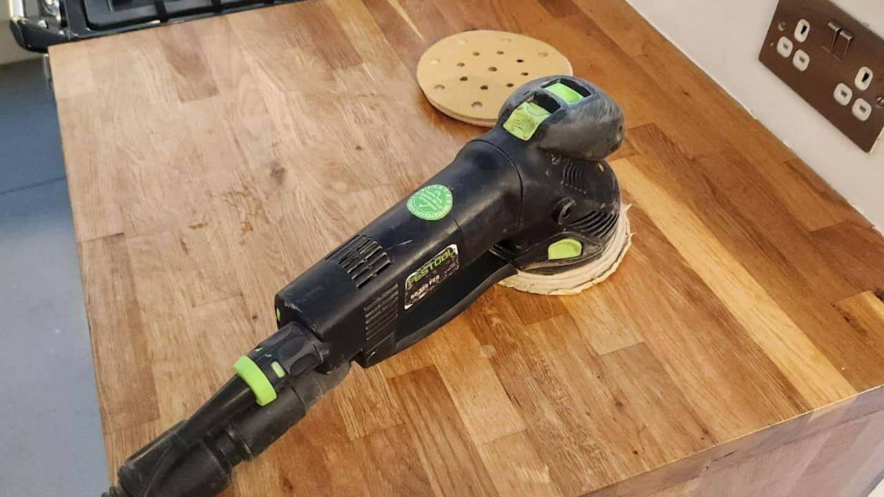 Worktop Refinishing in Tottenham with a Festool sander on an oak butcher-block kitchen worktop above a smooth grey resin kitchen floor