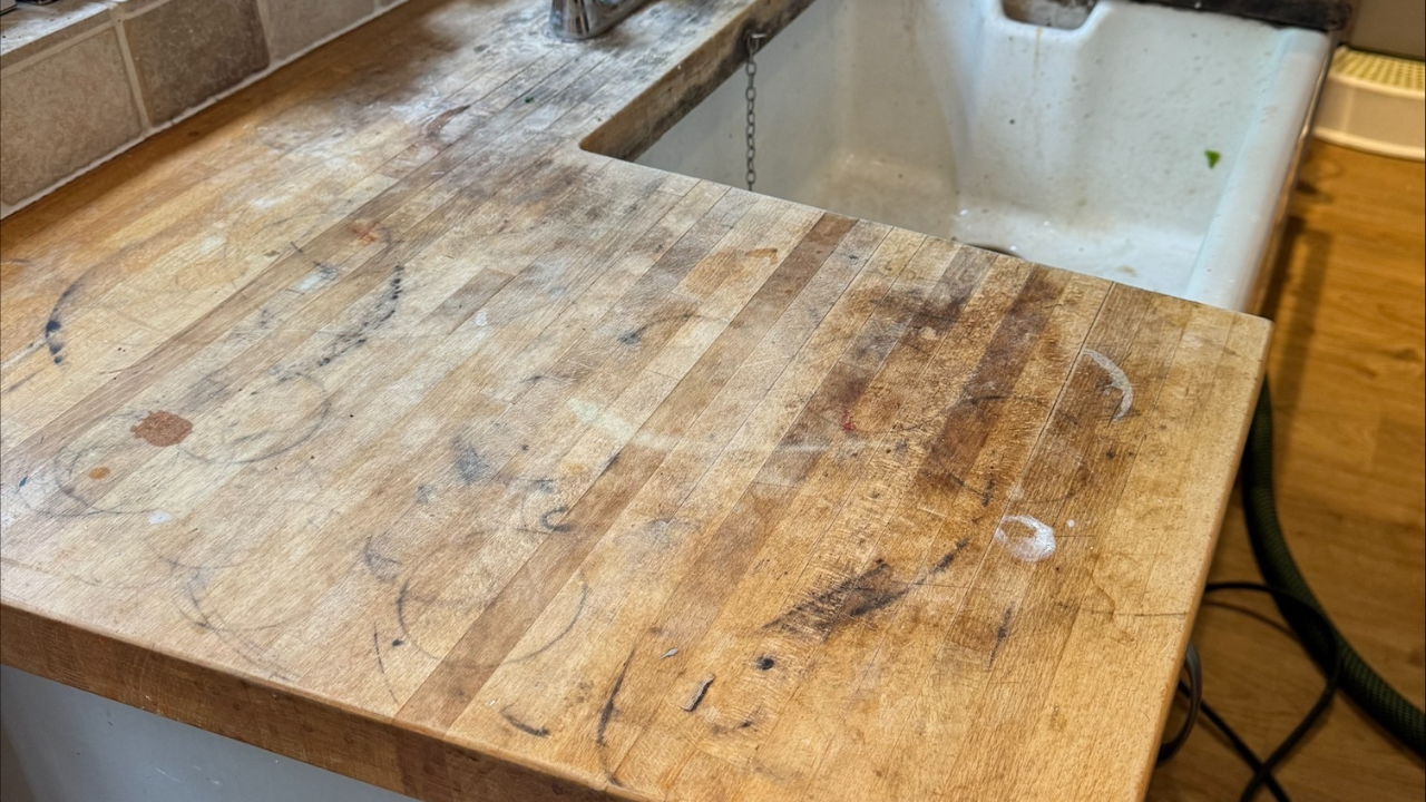 Worktop Refinishing in Tottenham showing a worn solid oak butcher-block kitchen worktop above a ceramic tile floor before restoration
